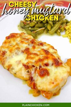 a white plate topped with cheesy chicken covered in cheese next to green beans