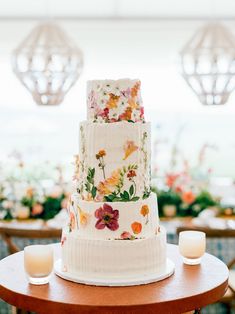 a wedding cake with flowers on it sitting on a table in front of some candles