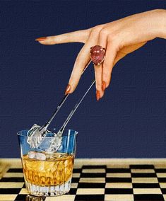 a woman's hand reaching for an object in a glass filled with liquid on top of a checkered table