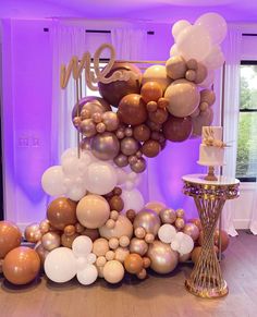 a table topped with lots of balloons in front of a purple lit room filled with windows