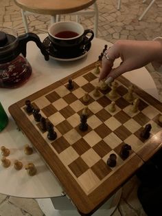 a person playing chess on a table with a cup of tea and kettles in the background