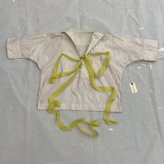 a white shirt with yellow ribbon tied around it on a gray surface next to a tag