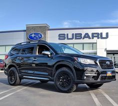 a black subaru suv parked in front of a subaru dealership with the subaru logo on it