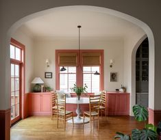 an archway leads into a dining room with pink painted walls and wooden flooring, along with large windows that have shutters open to let in natural light