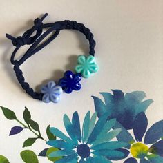 a bracelet with flowers and beads is shown on a white surface next to a blue flower