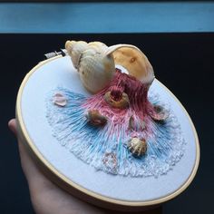 a hand holding a cross stitch project with seashells on it