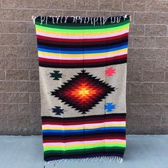 a multicolored blanket hanging up against a brick wall