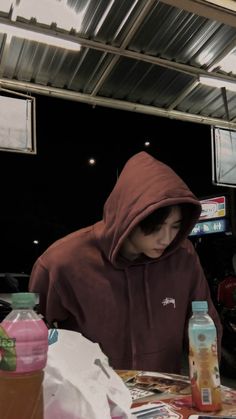 a person sitting at a table with drinks in front of him and wearing a hoodie