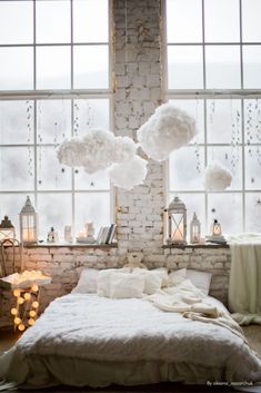 a bedroom with brick walls and large windows is decorated in white linens, hanging from the ceiling