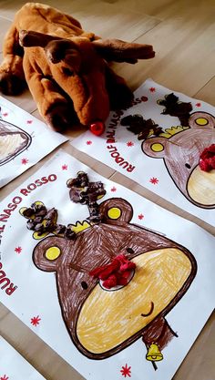 three children's handmade christmas cards on the floor with a stuffed animal in the middle