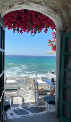 an open door leading to the beach with red flowers on it and water in the background