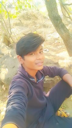 a young man sitting on the ground next to a tree