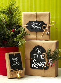 three presents wrapped in brown paper and tied with twine, sitting next to a potted christmas tree