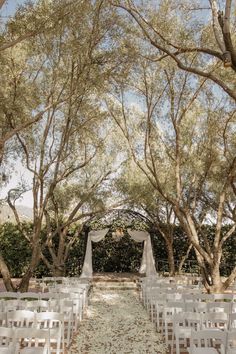 an outdoor ceremony with white chairs and trees