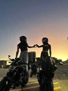 two women standing next to each other on motorcycles