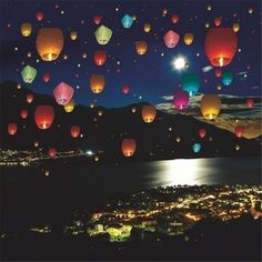 many colorful lanterns floating in the air over a city at night with lights on them