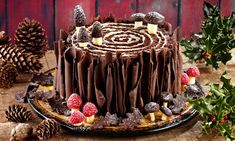 a chocolate cake sitting on top of a wooden table next to pine cones and berries