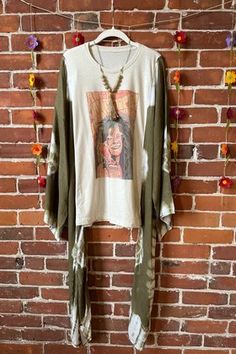 a woman's shirt hanging on a brick wall next to a flowery garland