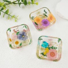 three glass trays with flowers painted on them sitting next to a flower plant and white towel