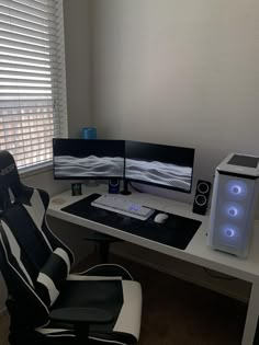 a computer desk with two monitors and a keyboard on it, in front of a window