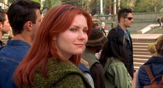 a woman with red hair standing in front of some stairs and people looking at the camera