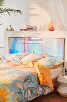 a bed with colorful comforters and pillows in a bedroom next to a plant on the wall