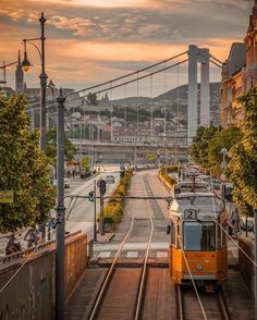 an orange train traveling down tracks next to tall buildings and a street light in the distance