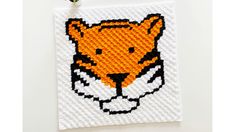 an orange and white tiger head is on a piece of woven material, with a small green plant in the corner