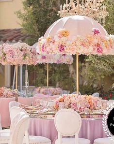 a table set up for a wedding with an umbrella and flowers on the tables in front of it