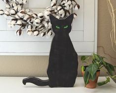 a black cat with green eyes sitting next to a wreath