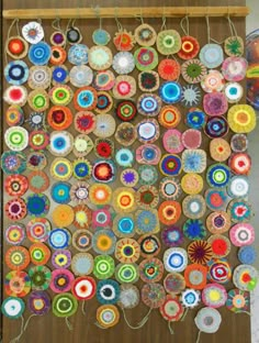 a wall hanging made out of different colored circles and yarns on a wooden board