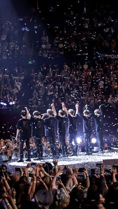 the backs perform on stage with their arms in the air as confetti is thrown around them