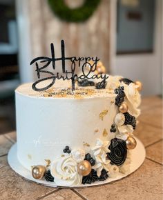 a white cake with black and gold decorations on it that says happy birthday written in frosting