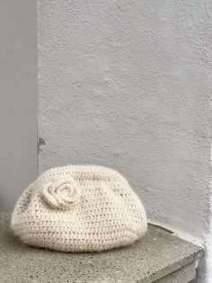 a white knitted hat sitting on top of a cement bench next to a wall