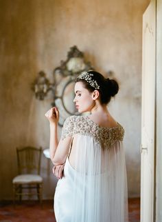 a woman in a white dress is standing near a wall and looking at the mirror