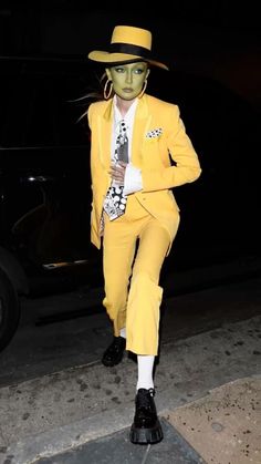 a man in a yellow suit and hat is walking down the street with his hand on his hip