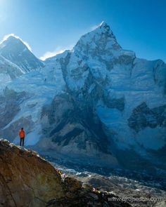 a man standing on top of a mountain with snow covered mountains in the back ground