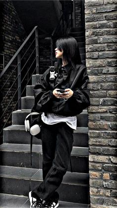 a woman with black hair standing in front of some stairs looking at her cell phone