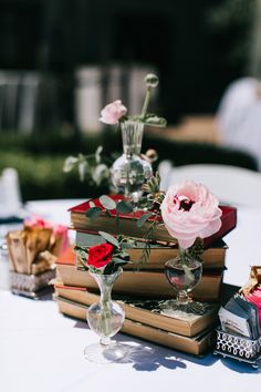 a stack of books sitting on top of a table next to vases filled with flowers