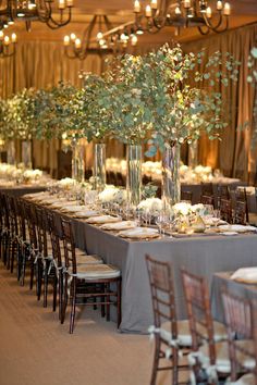 a long table is set with tall vases filled with flowers and greenery for an elegant wedding reception