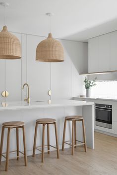 three wooden stools sit in front of an island with white countertops and cabinets