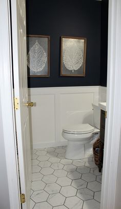 a white toilet sitting inside of a bathroom next to a sink and mirror with two paintings on the wall