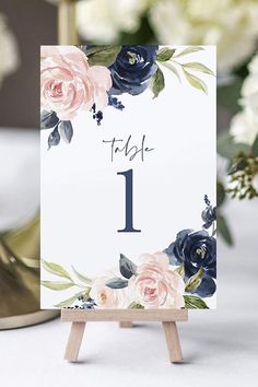 a table number with pink and blue flowers on it, next to an easel