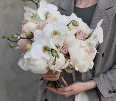 a woman holding a bouquet of white flowers in her hands and wearing a gray jacket