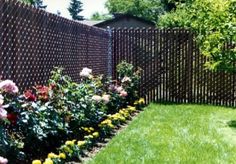 a garden with lots of flowers next to a fence and green grass in front of it