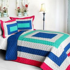 a bed covered in a blue and pink quilt next to a window with potted plants