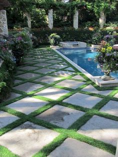 an outdoor swimming pool surrounded by greenery and stone pavers walkways that lead into the back yard