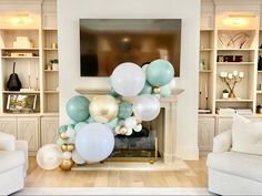 a living room filled with white couches next to a fire place covered in balloons