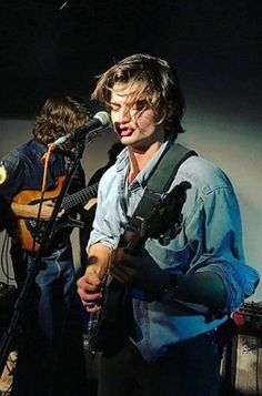 a man playing guitar while singing into a microphone and another person standing next to him