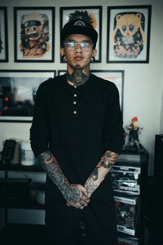 a man with tattoos and piercings standing in front of some pictures on the wall